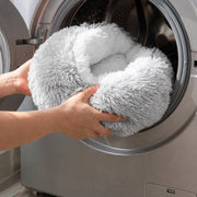 Gray PETNEST Shell-Shaped Plush Cave Bed being placed into a front-loading washing machine
